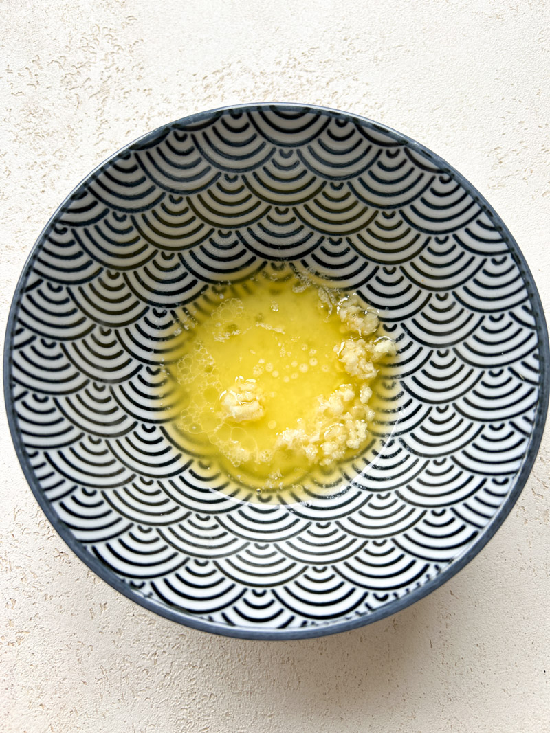Melted butter and pressed garlic on a blue bowl.