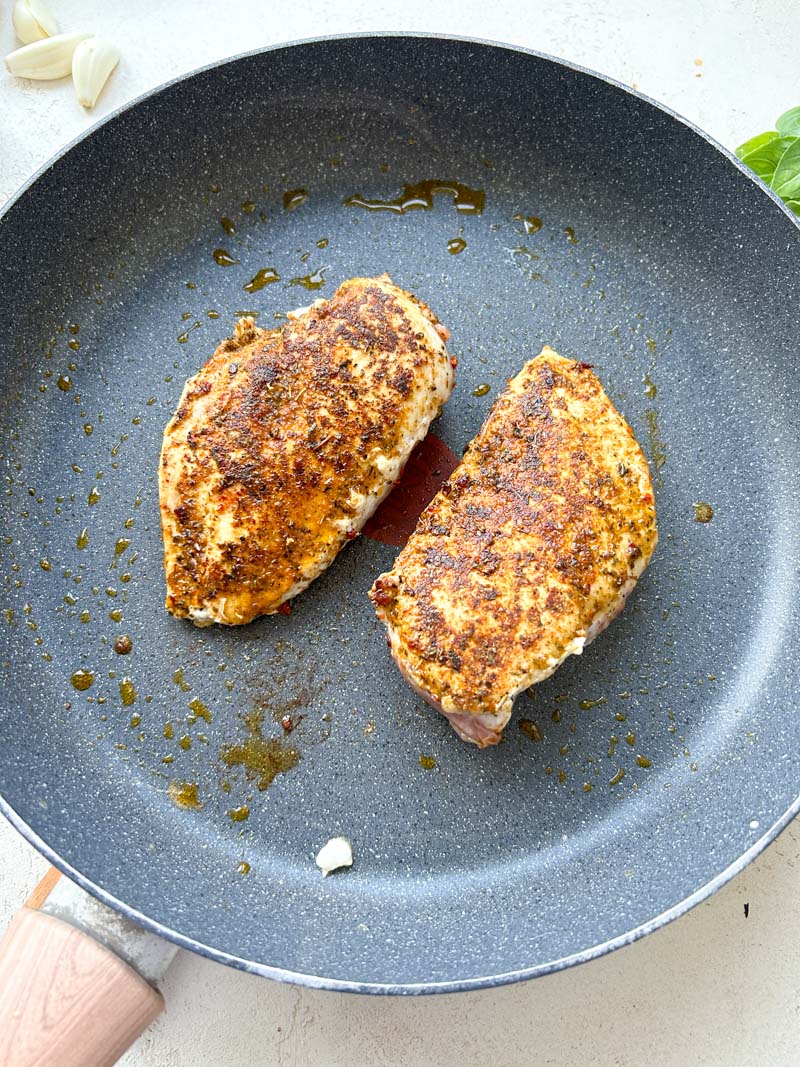 Two cooked chicken breasts in a frying pan.