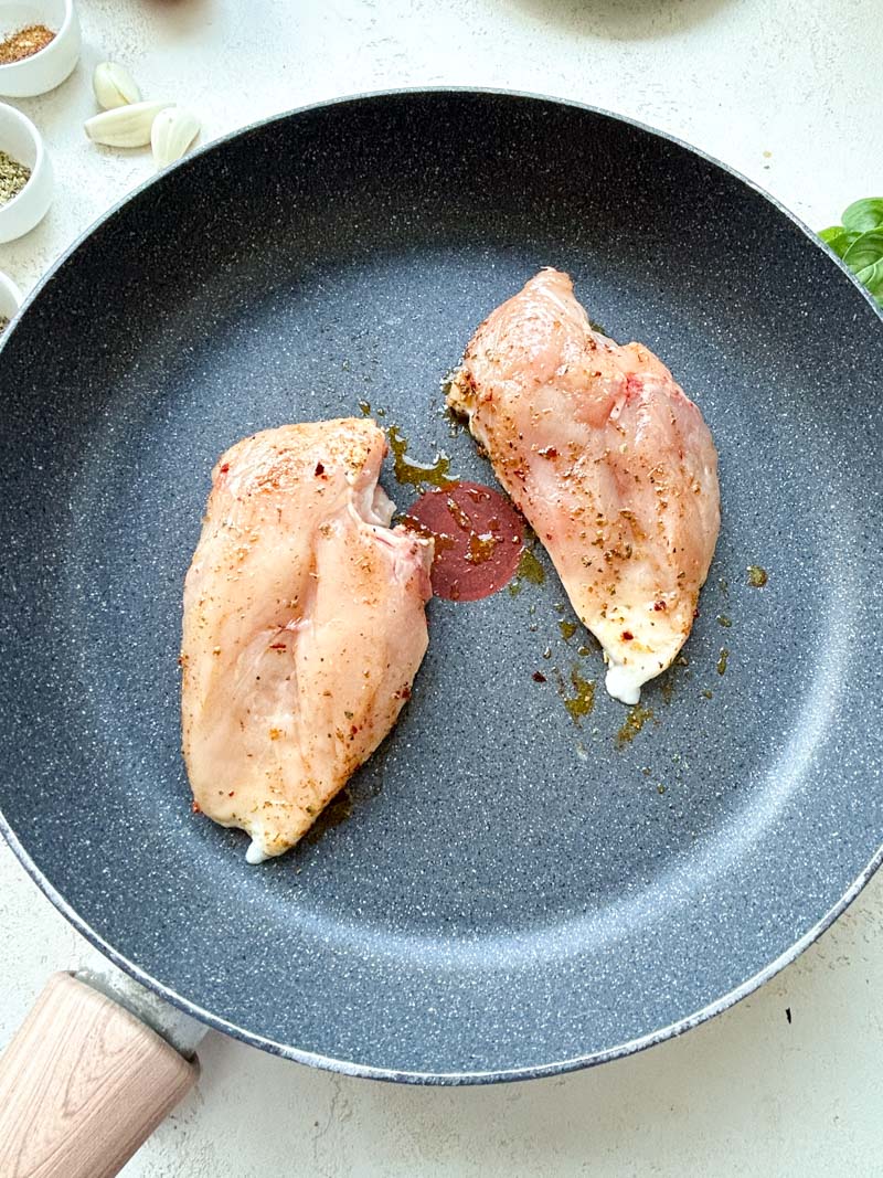 Two uncooked chicken breasts in a frying pan.