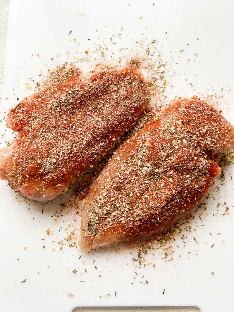 Chicken breasts with Blackening seasoning on a white cutting board.