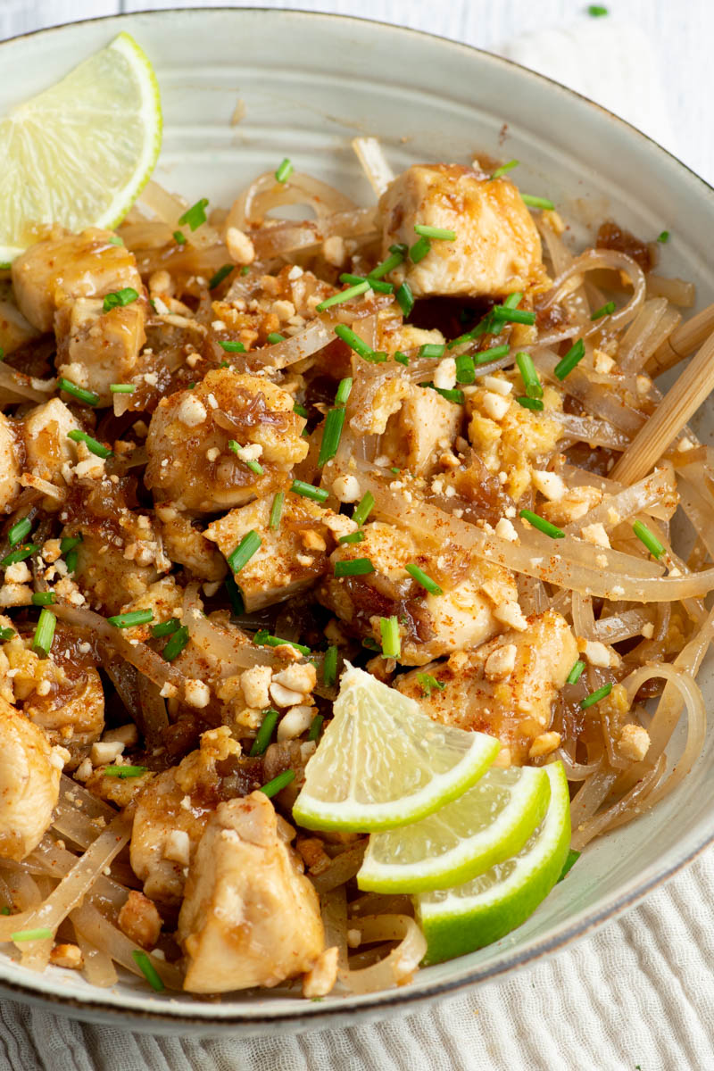 Chicken Pad Thai in a beige bowl with lime wedges and wooden chopsticks.