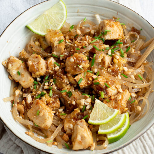 Chicken Pad Thai in a beige bowl with lime wedges and wooden chopsticks.