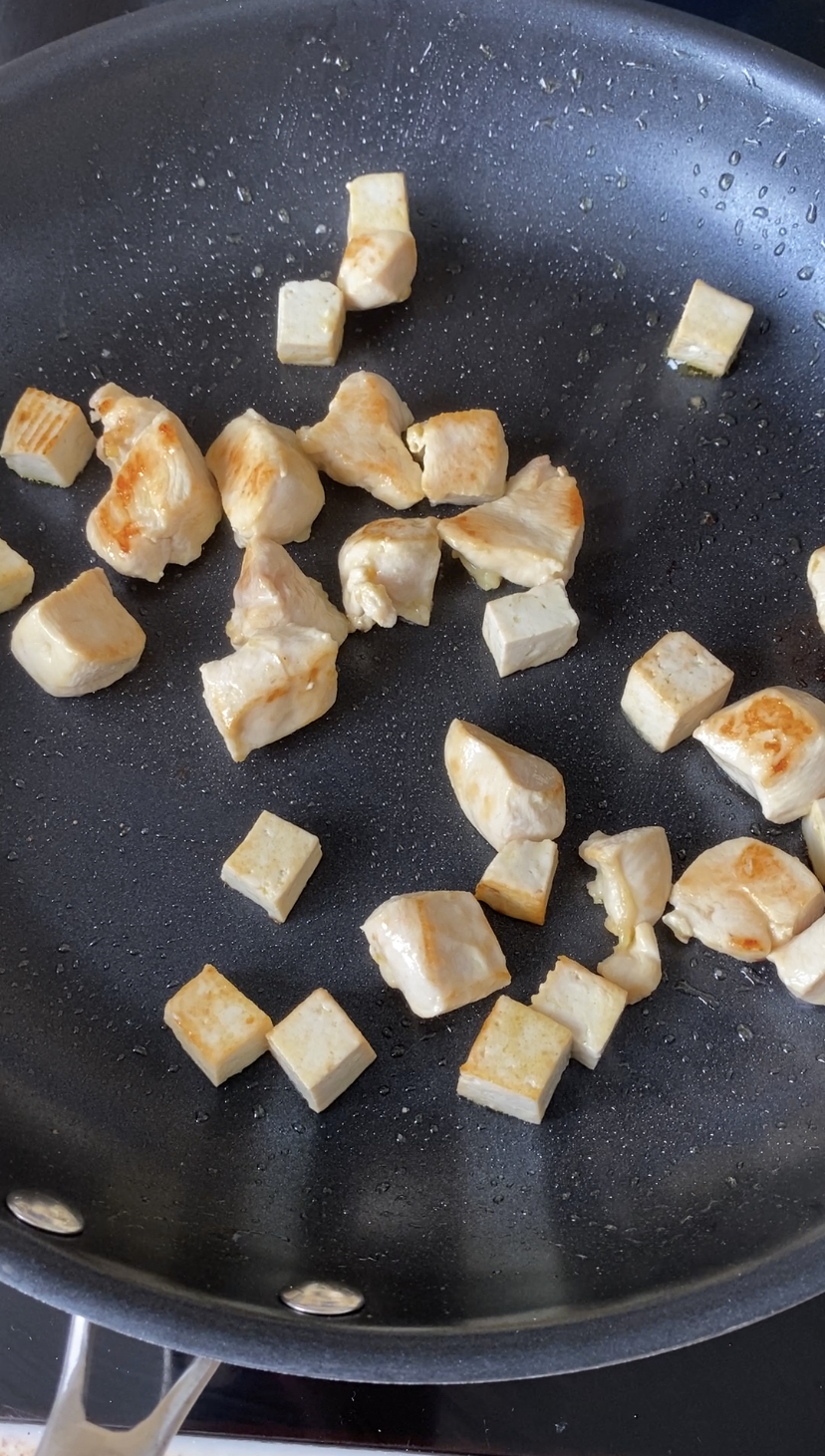 Cubes de poulet et de tofu cuits dans une grande poêle noire.