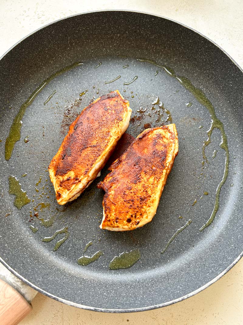 Seasoned and cooked chicken breasts in a large skillet with olive oil.