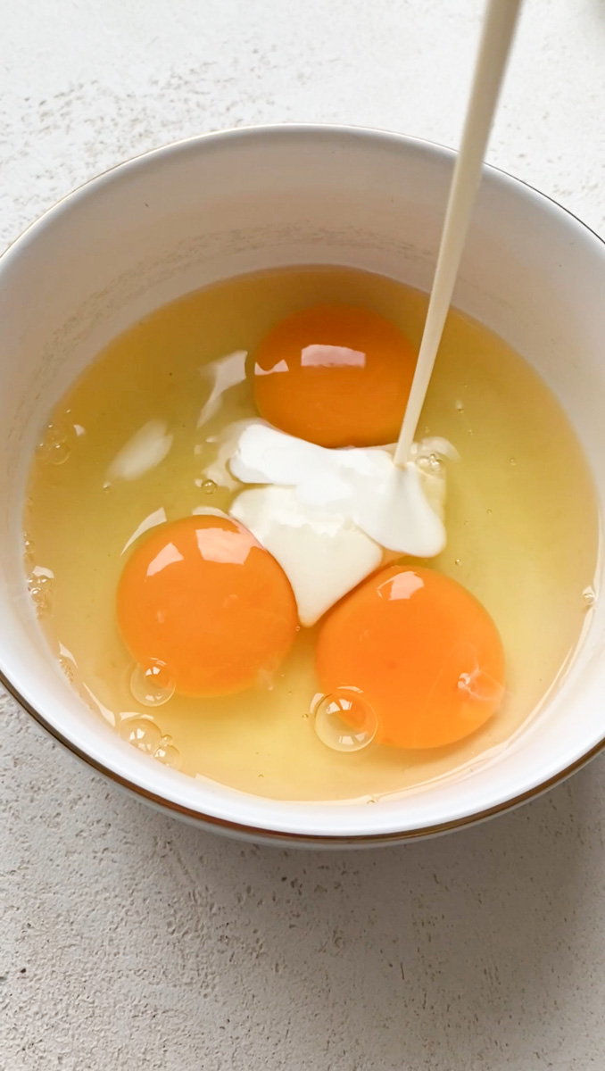 Eggs in a white bowl with heavy cream poured in.