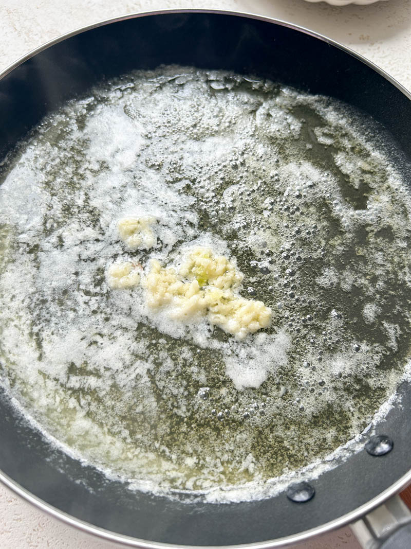 Pressed garlic added to the frying pan of melted butter.