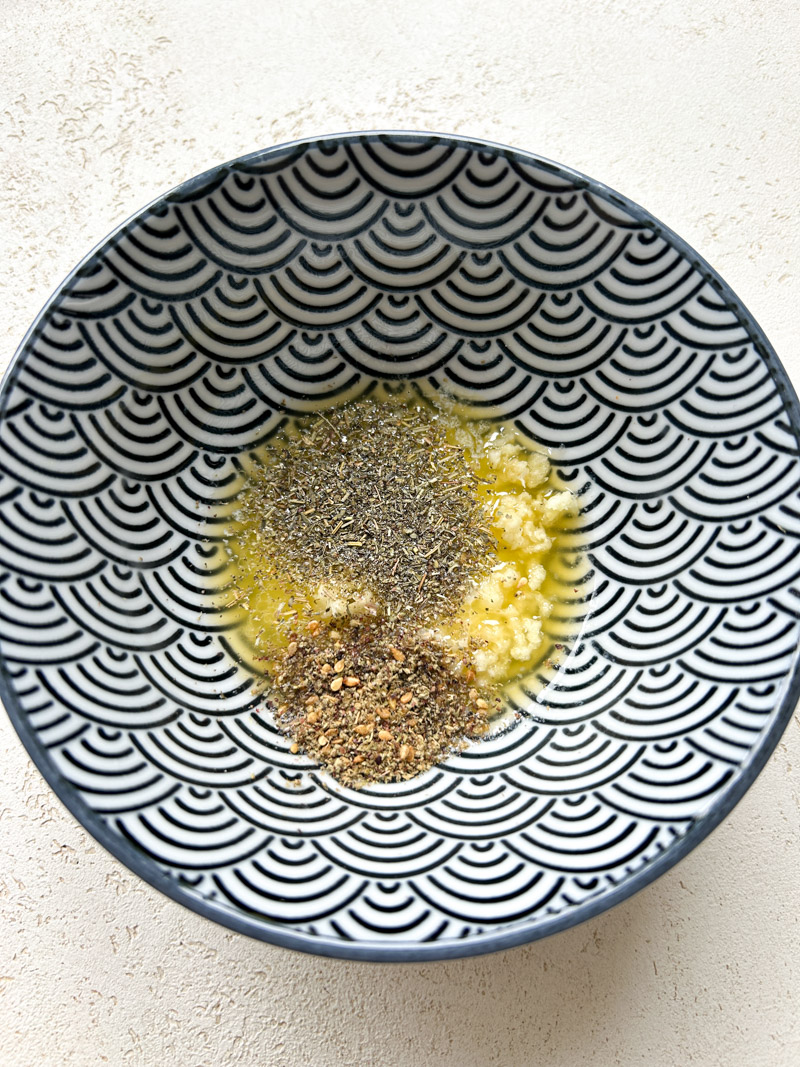 Herbs added to the blue bowl of melted butter and pressed garlic.