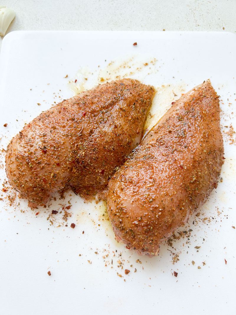 Mélange italien sur deux filets de poulet, sur une planche à découper blanche.