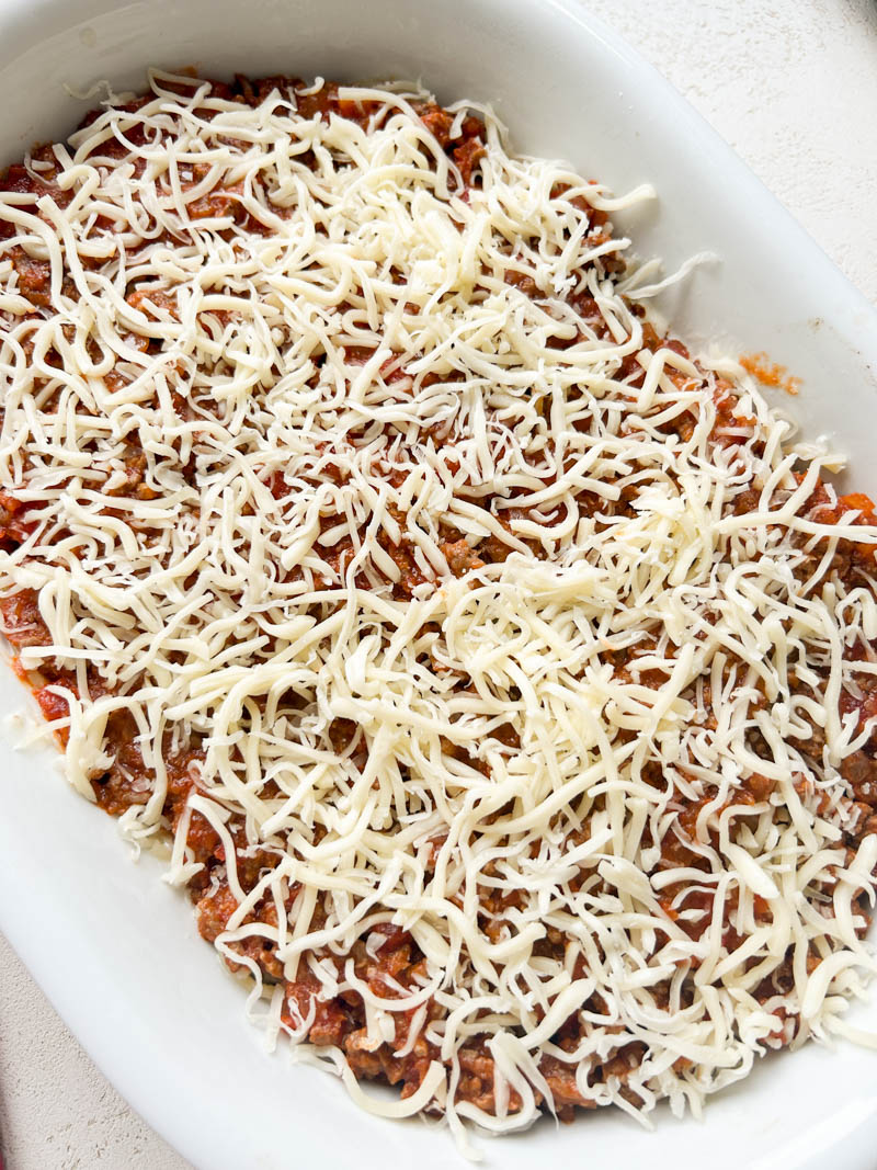 Shredded mozzarella cheese on top of the meat marinara, in a white baking dish.