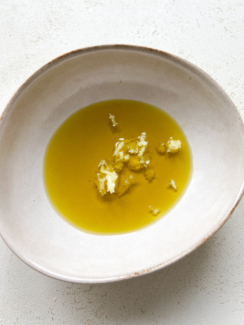 Beige bowl filled with olive oil and pressed garlic.