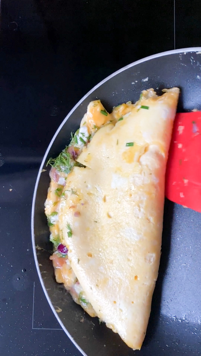 La spatule rouge finissant de replier l'omelette dans la poêle.
