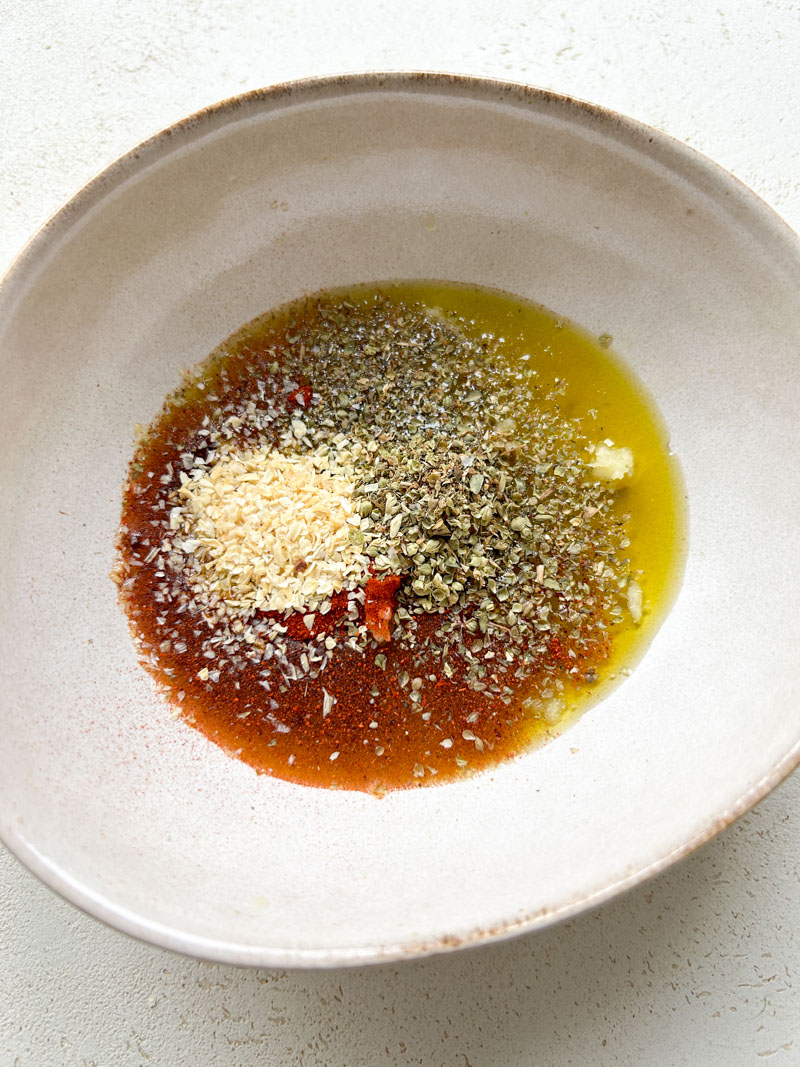 Onion powder and oregano added to the bowl of olive oil.