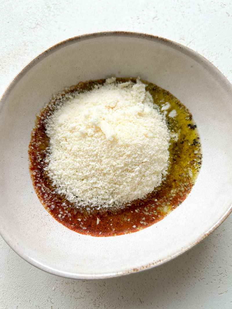 Du parmesan fraîchement râpé ajouté au bol d'huile d'olive.