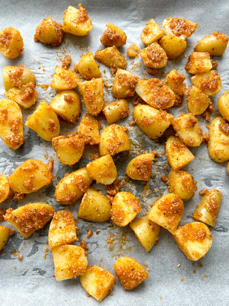 Potatoes coated with the Parmesan cheese mixture on a baking sheet lined with parchment paper.