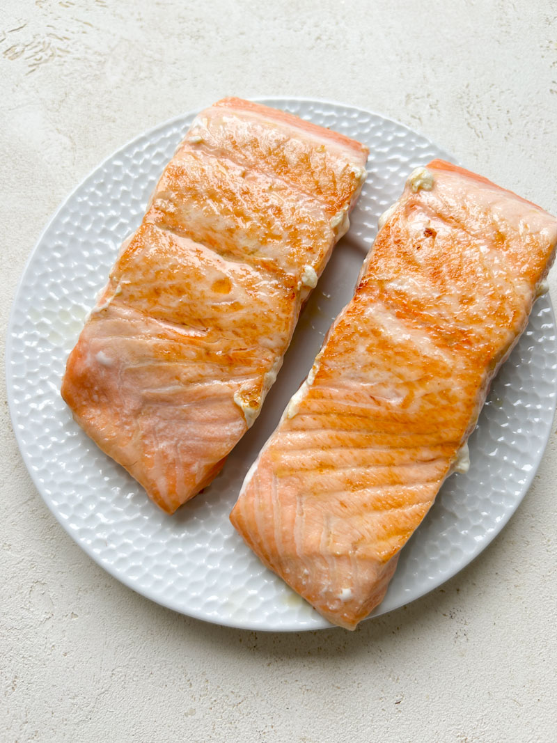 Two cooked salmon fillets in a white small plate.