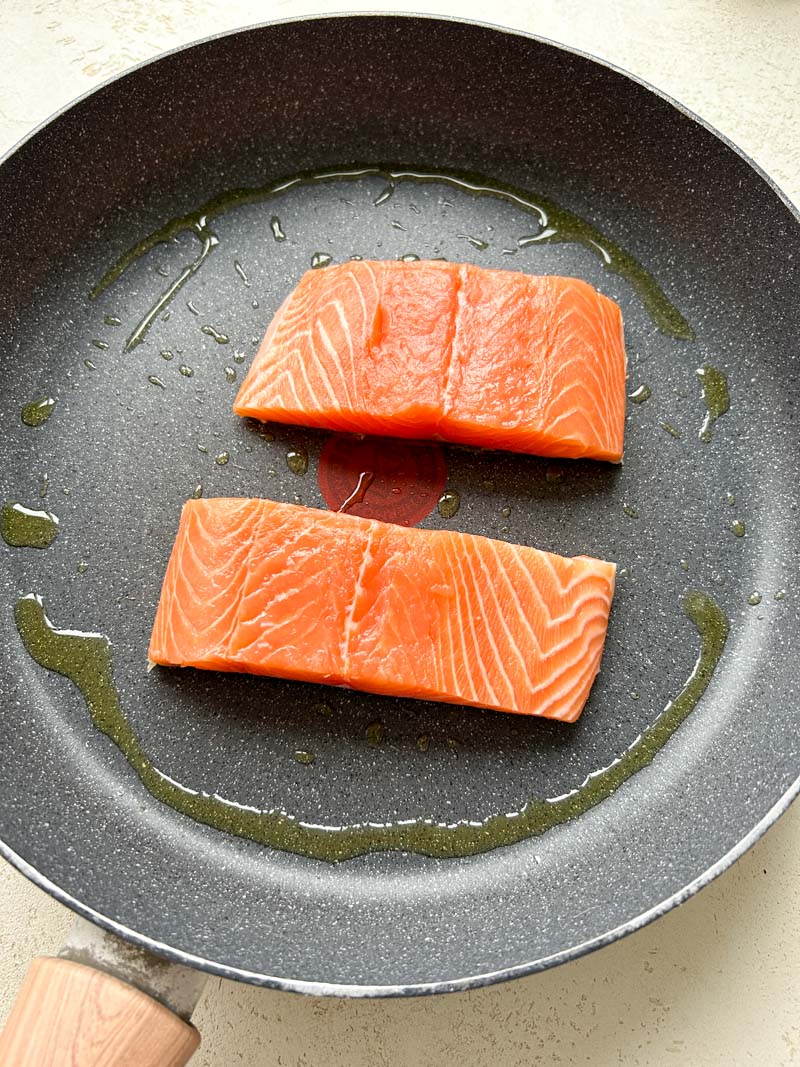 Two salmon fillets in a large pan with olive oil.