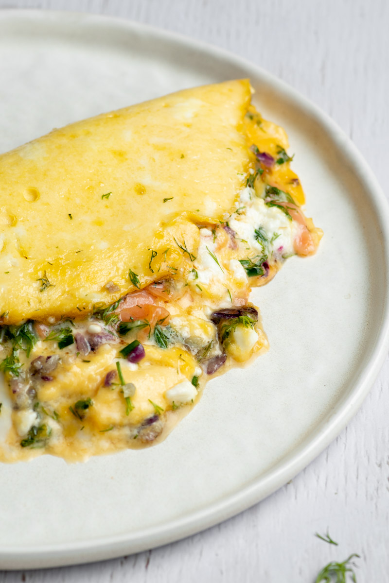 Smoked salmon omelette in a white plate, with feta cheese, red onion and fresh herbs.