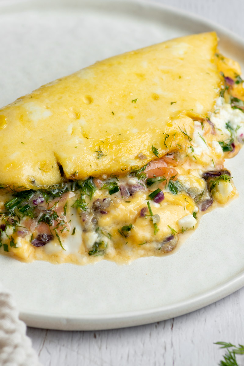Omelette avec du saumon fumé, de la feta, de l'oignon rouge et des herbes fraîches dans une assiette blanche.