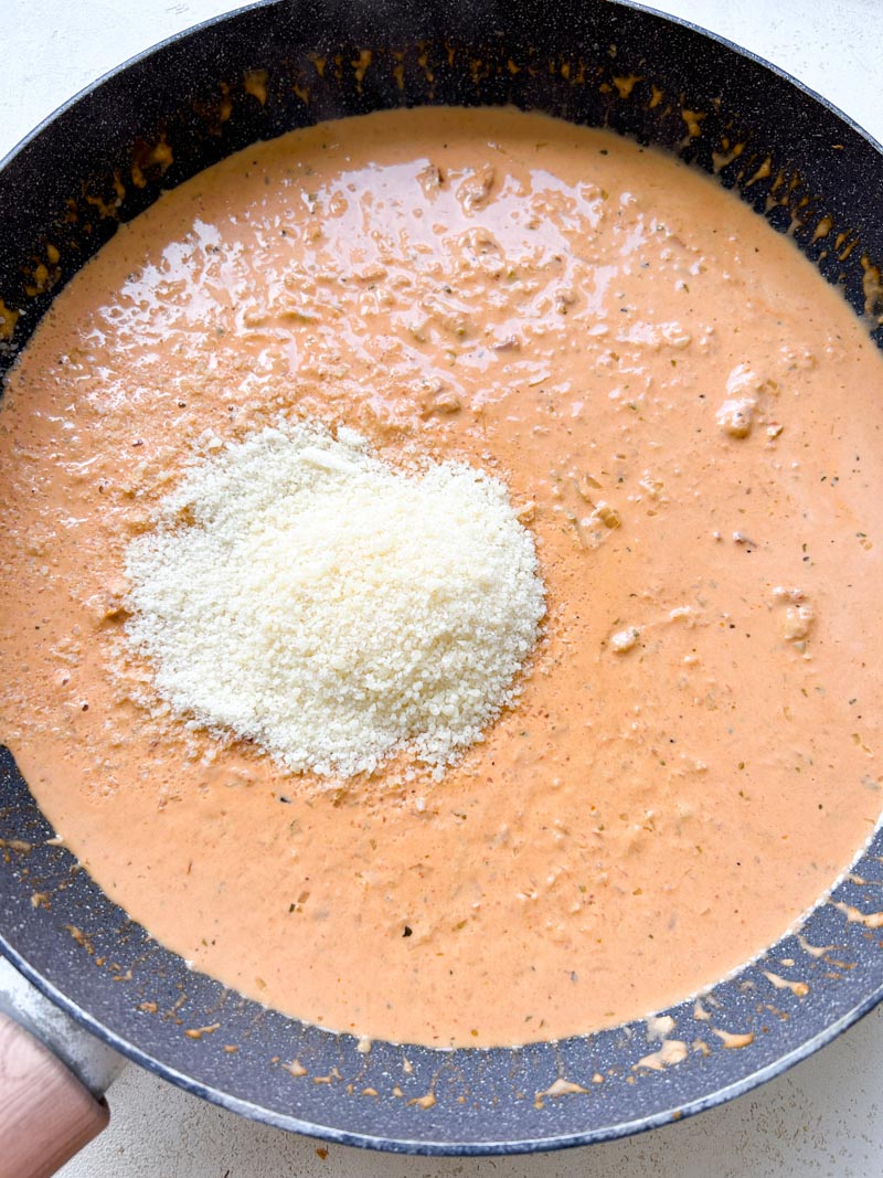 Freshly grated Parmesan cheese added to the skillet of red sauce.