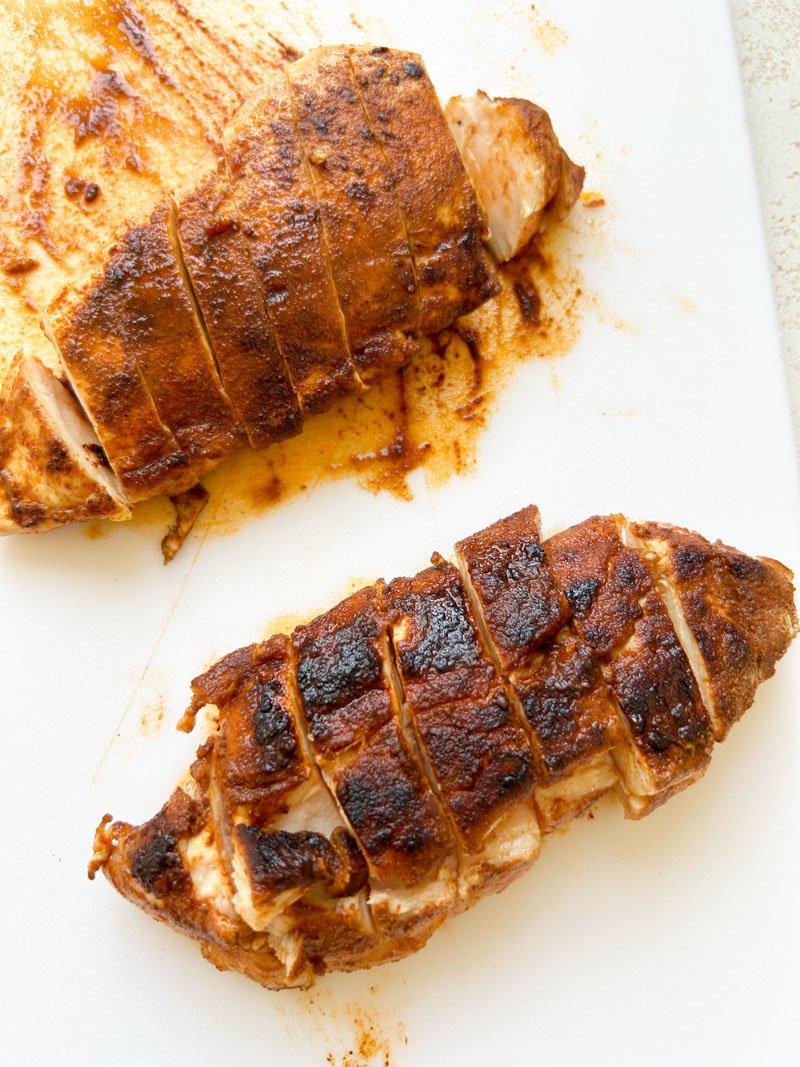 Sliced chicken breasts on a white cutting board.