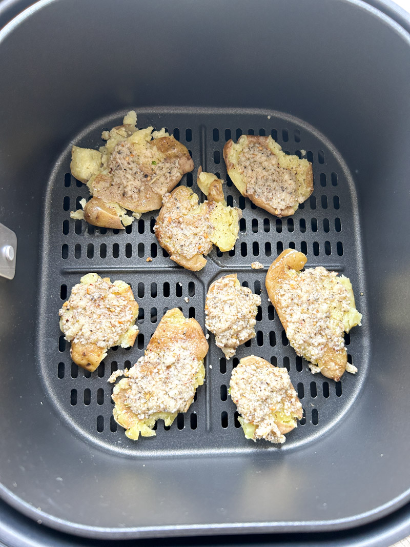 Smashed potatoes, brushed with mixture, in the Air Fryer basket before cooking.