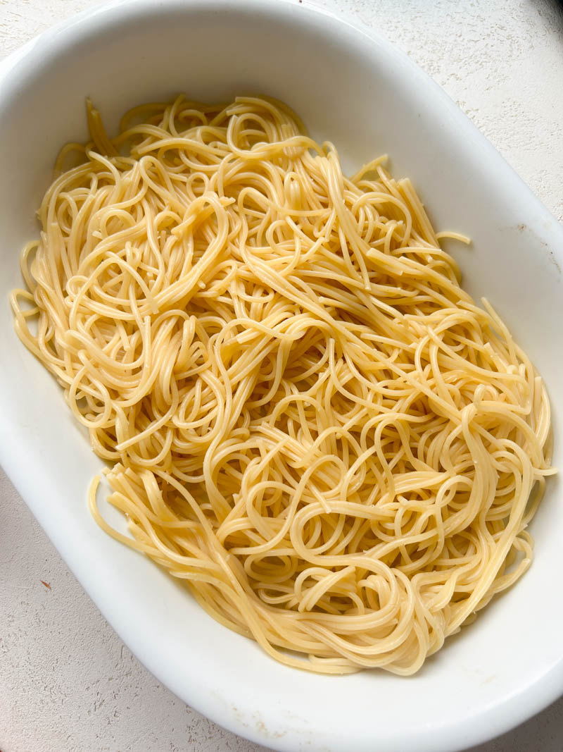 Cooked spaghetti placed in a white baking dish.