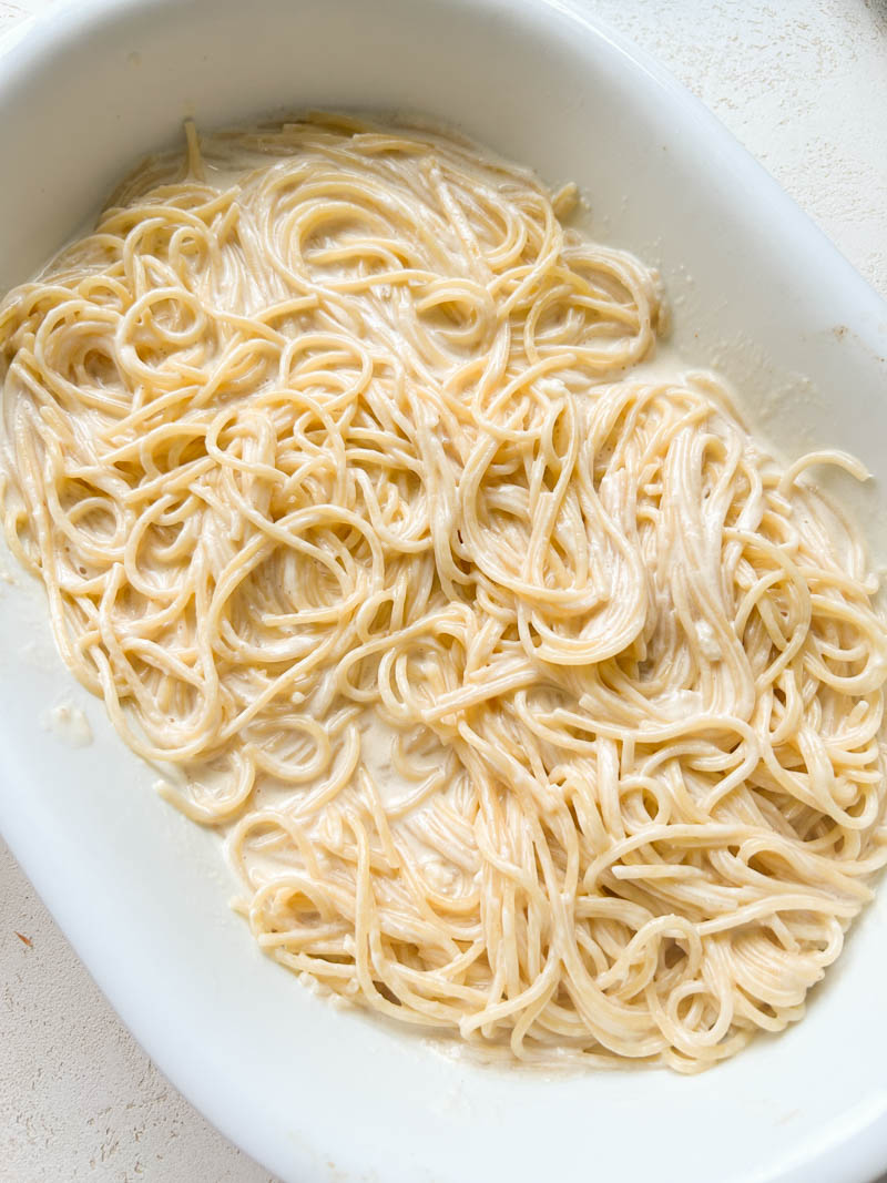 Spaghetti mixed with Alfredo sauce in a white baking dish.