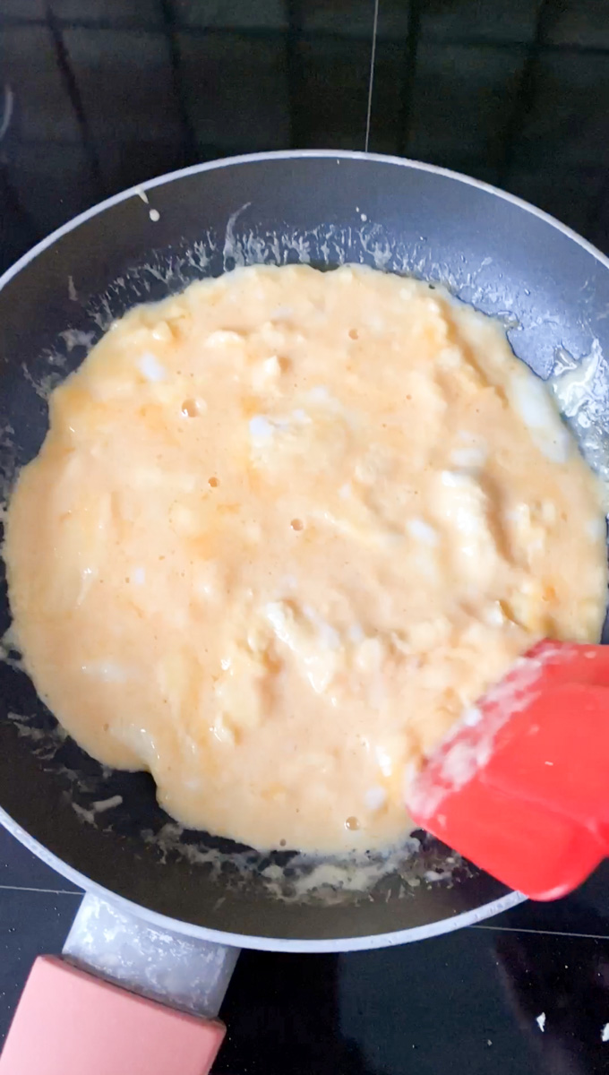 A red spatula scrambling the egg mixture.