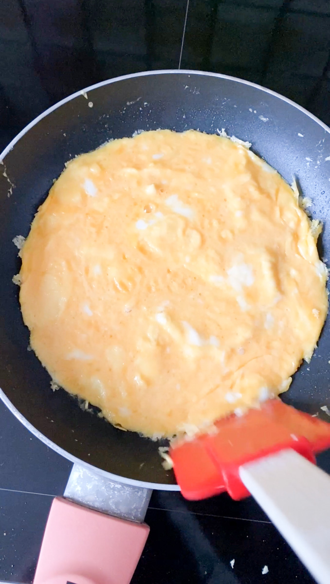 Omelette prête, avec une spatule rouge qui détache les bords.