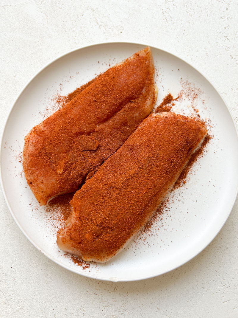 Spice mix on the chicken breasts, placed in a white plate.