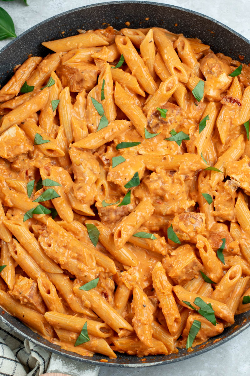 Creamy pasta with bites of chicken and freshly chopped basil in a large skillet.