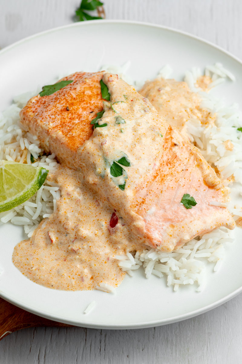 Salmon fillets in a white plate with a creamy coconut curry sauce.