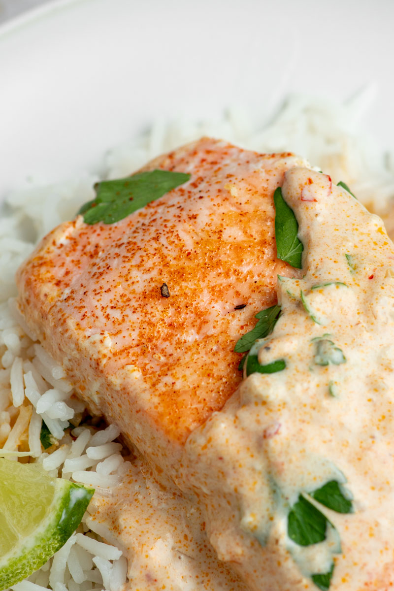 Salmon fillet in a white plate with a creamy coconut curry sauce.