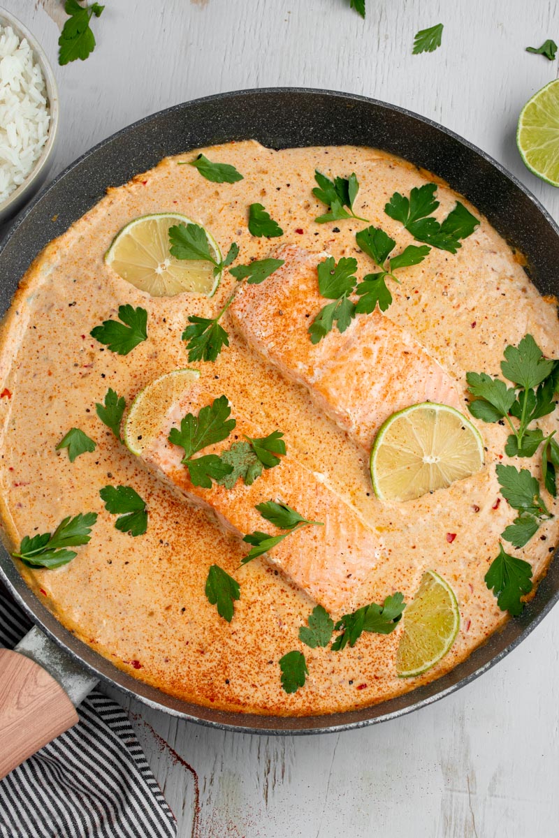 Salmon fillets in a large pan of creamy coconut curry sauce.