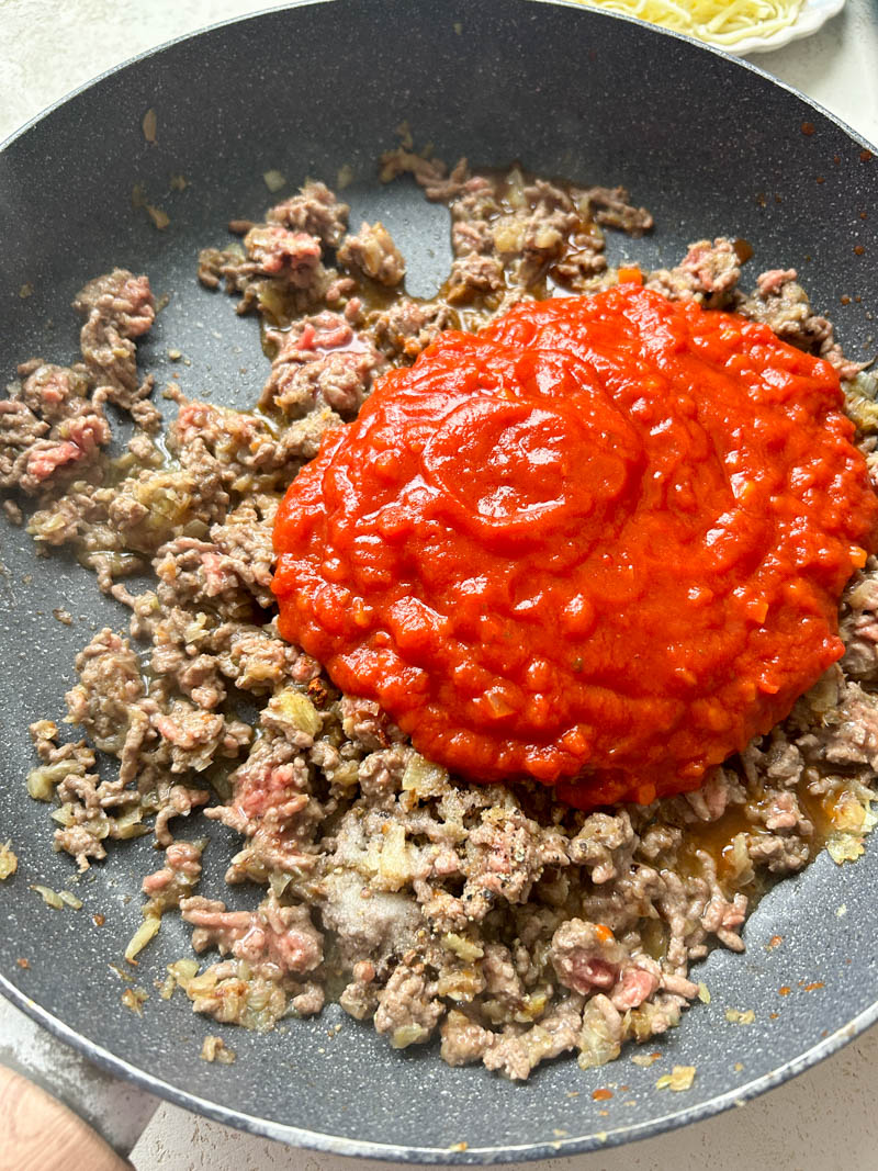 Tomato sauce added to the frying pan of cooked ground beef.