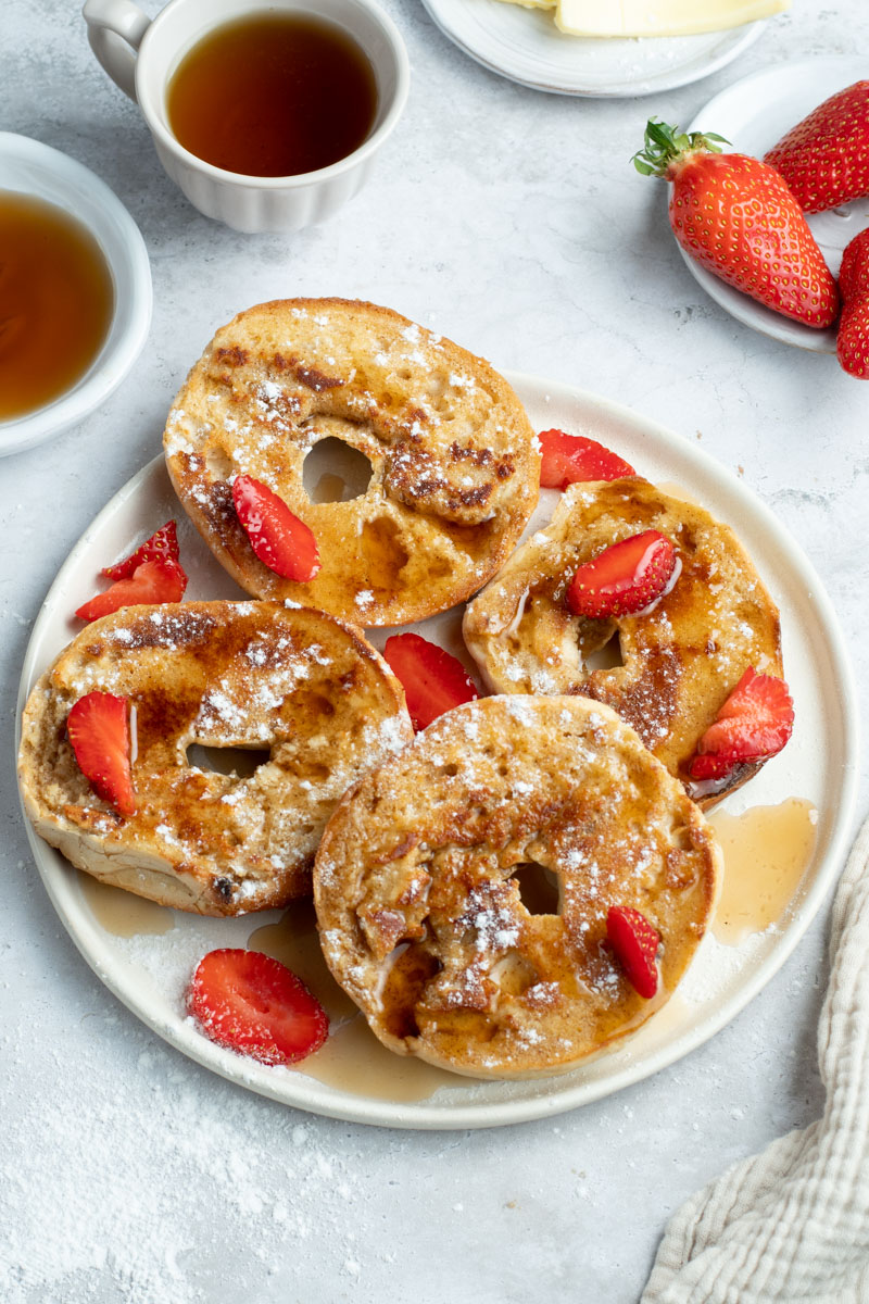 Bagel French toasts in a white plate with maple syrup and strawberries.