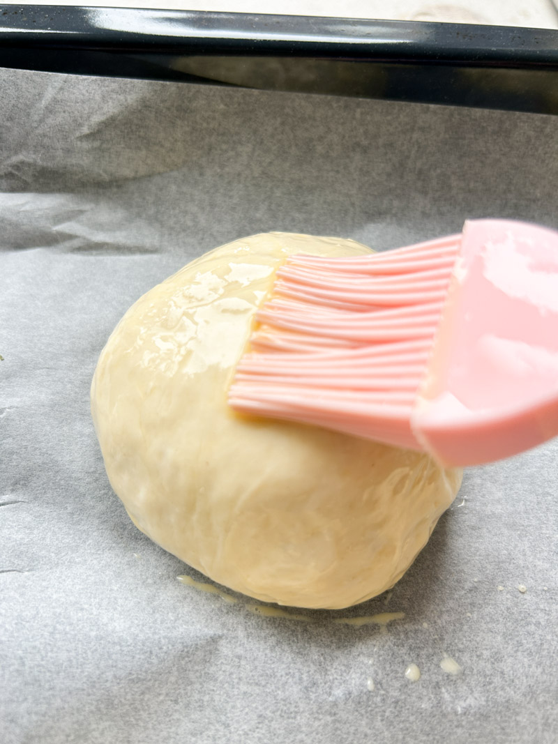Un pinceau en silicone rose badigeonne un pâton avec le mélange de lait et d'œuf.