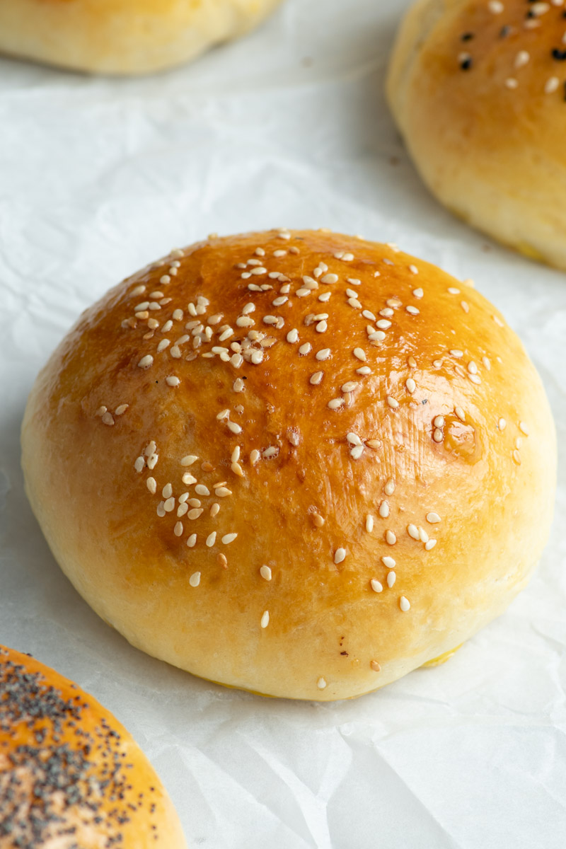 Brioche burger buns topped with sesame seeds on parchment paper.
