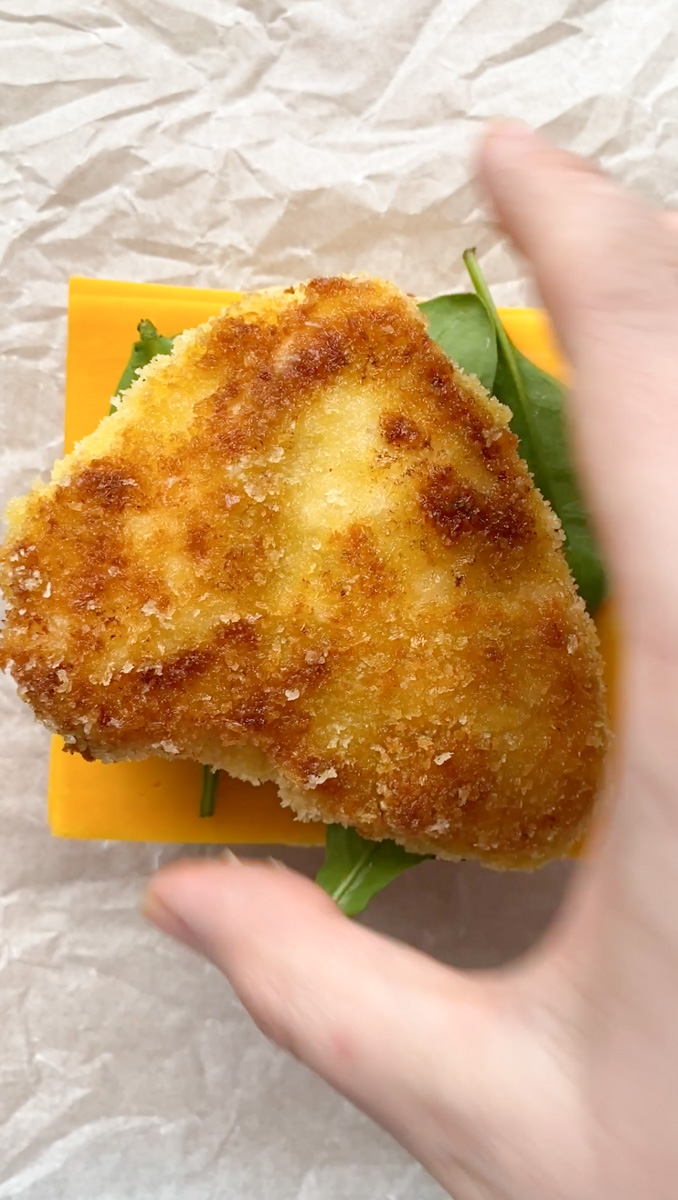 A hand placing the crispy breaded chicken on top of the baby spinach.