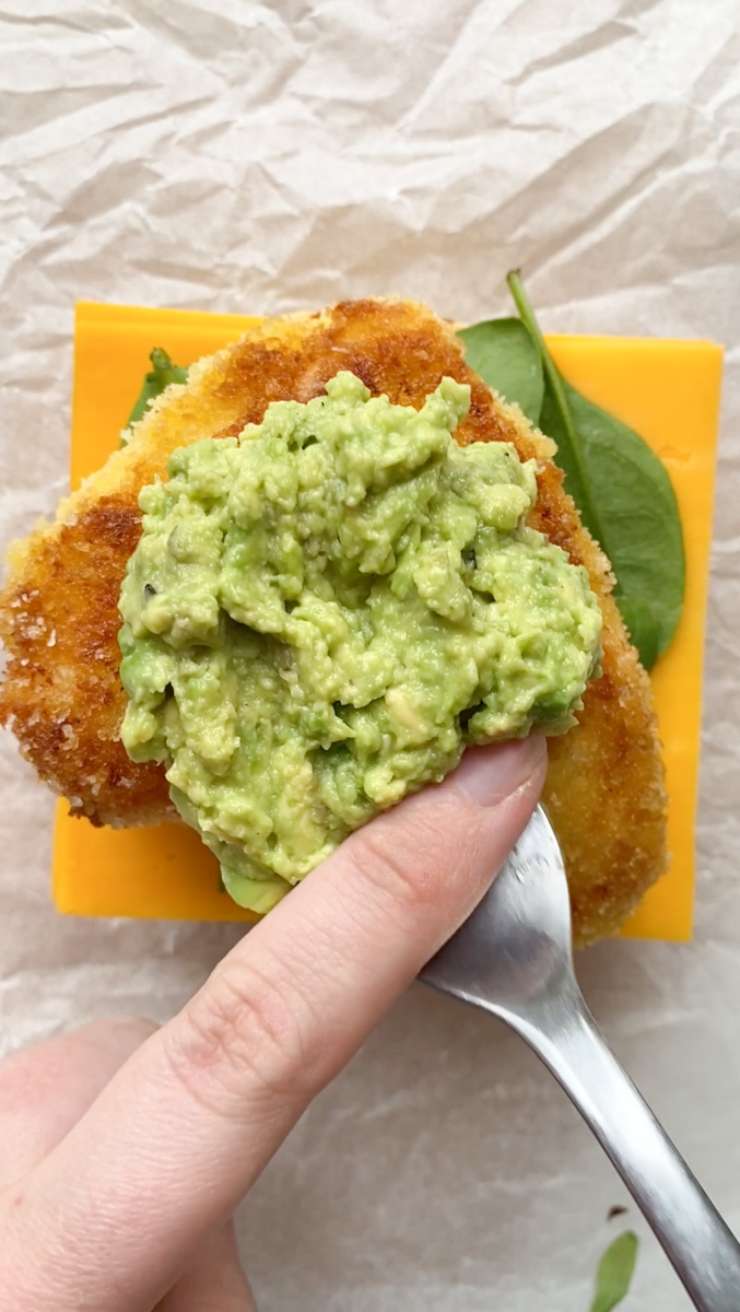 Mashed and seasoned avocado added by a fork on top of the crispy breaded chicken.