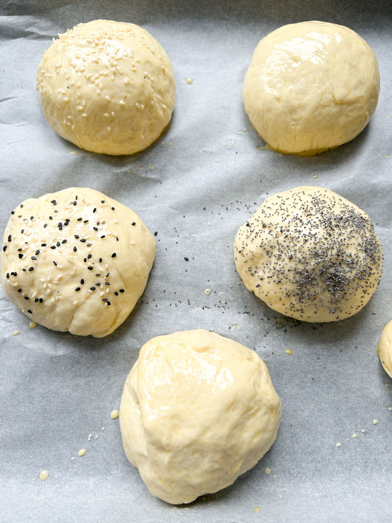 Brioche burger buns ready to be baked, with different toppings - sesame seeds, poppy seeds, etc...