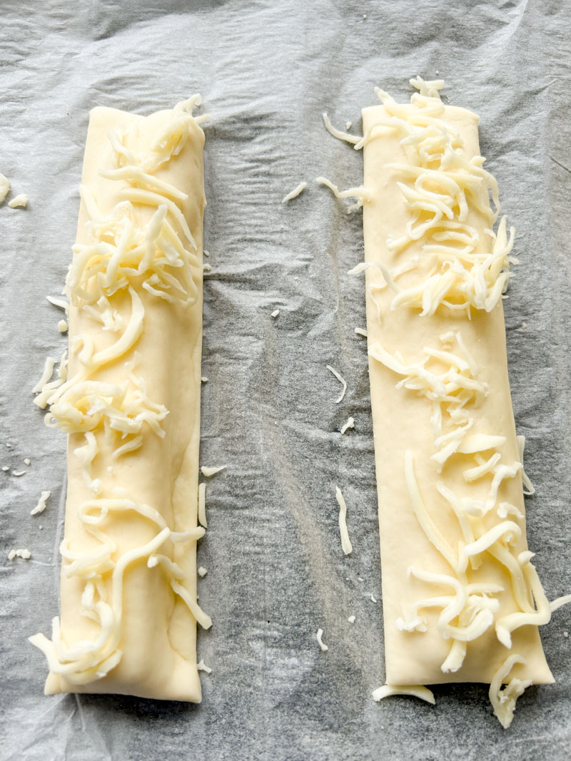 Mozzarella râpée est ajoutée sur les deux sticks, sur du papier cuisson.