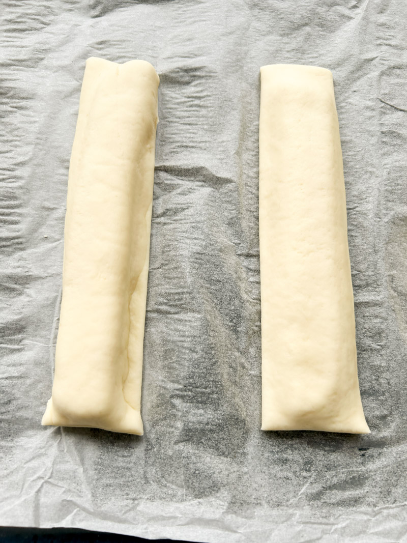 Two mozzarella cheese sticks placed on parchment paper.