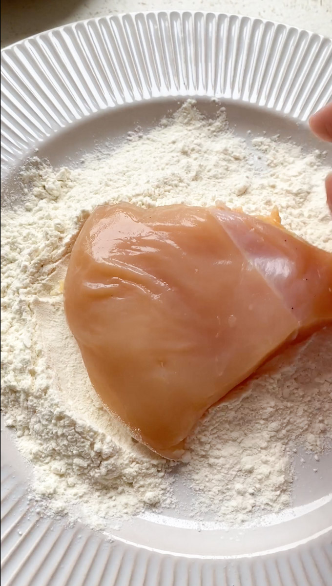 Piece of chicken breast in a plate full of flour.