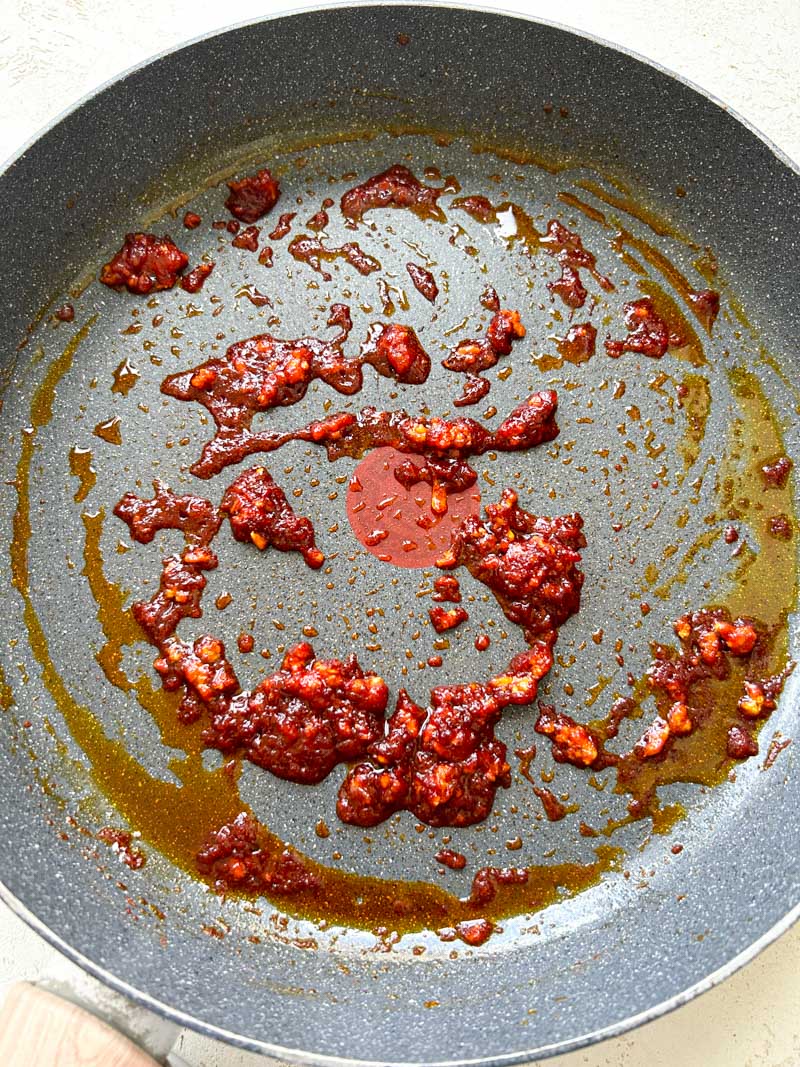 Cooked Gochujang mixed with the garlic in the skillet.