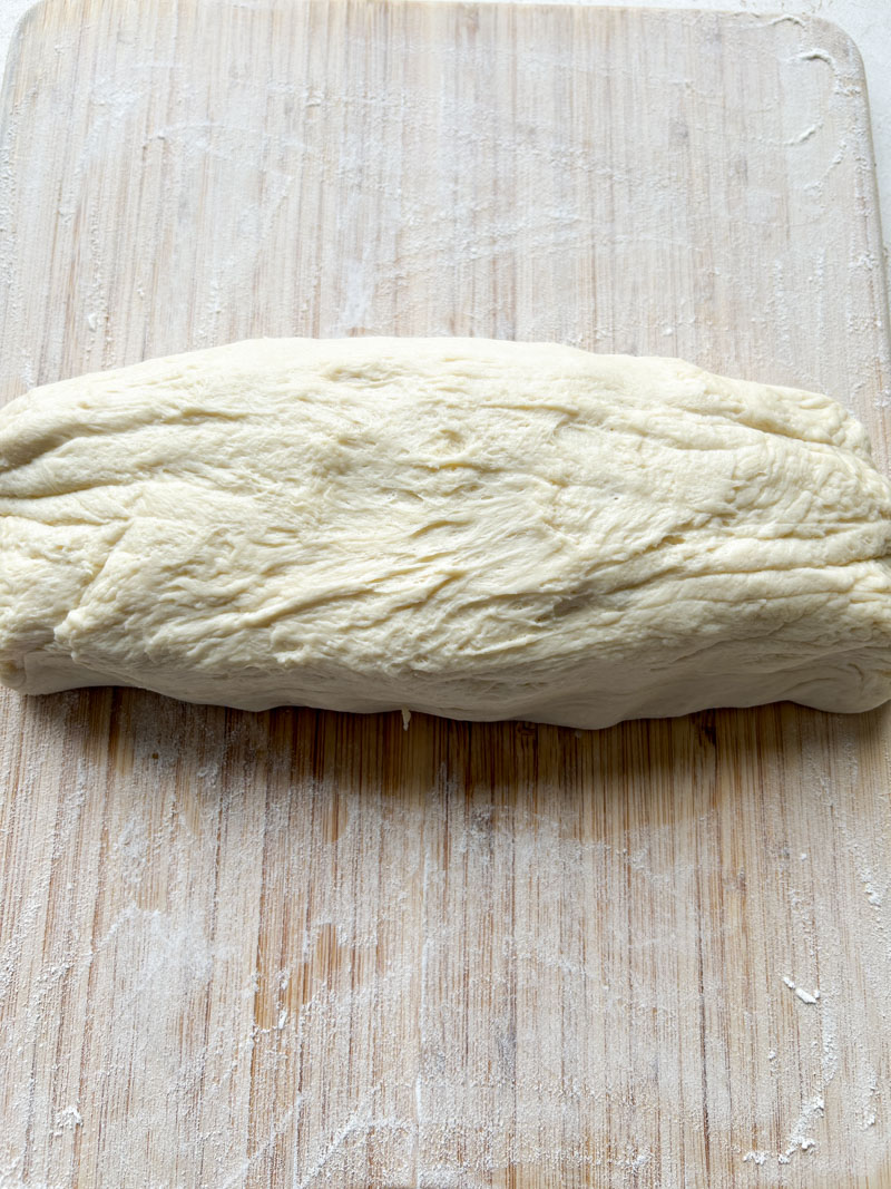 Pâte en forme de rectangle, prête à être découpée en petits pâtons.