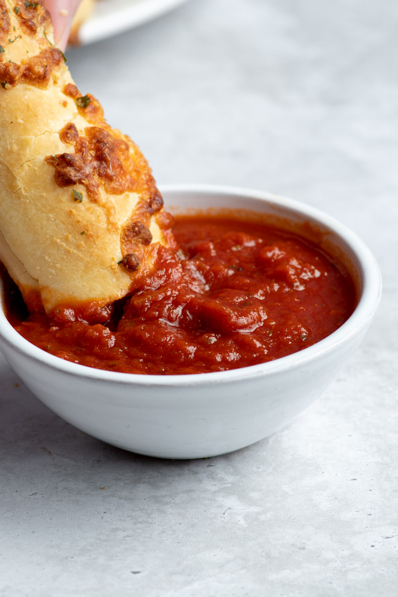 Une main plongeant un mozzarella stick dans un petit bol de sauce tomate blanc.