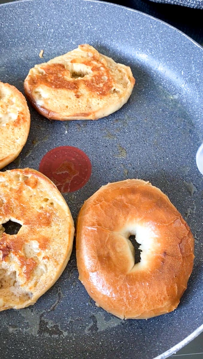 Four half bagels baking in a large pan with butter.