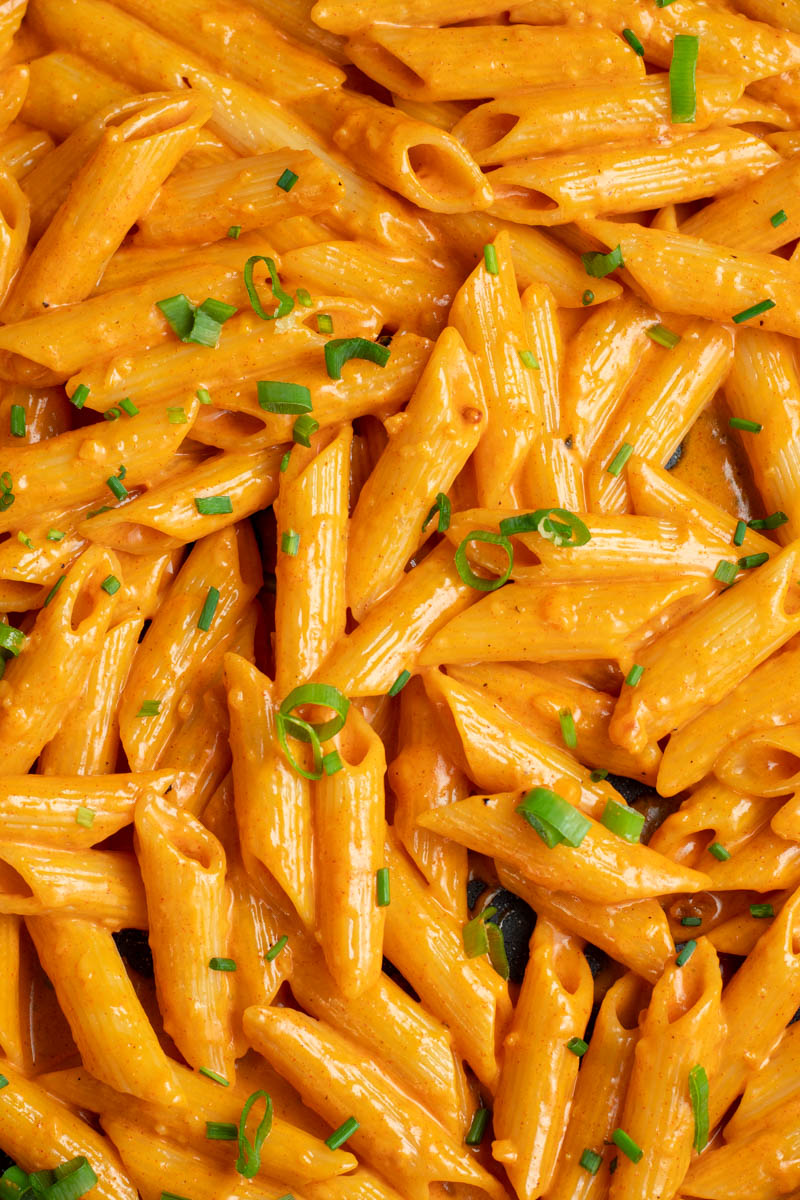 Creamy Gochujang pasta in a large skillet with spring onions and fresh chopped chives.