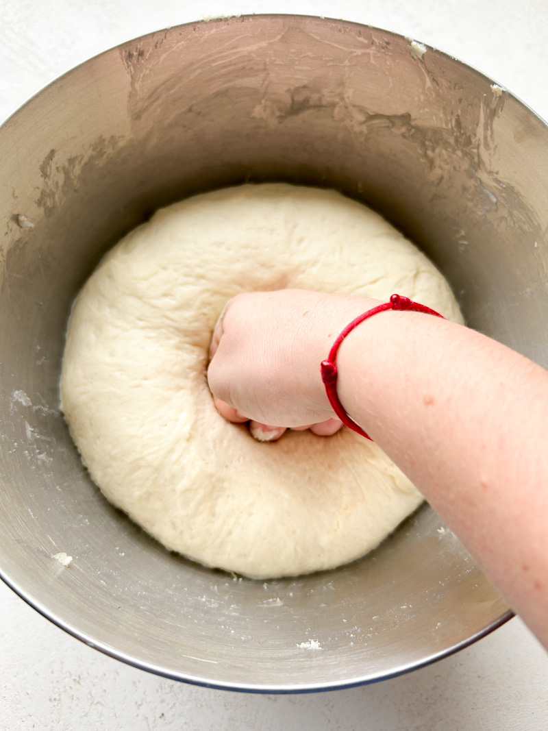 A hand punching out the air of the dough ball.